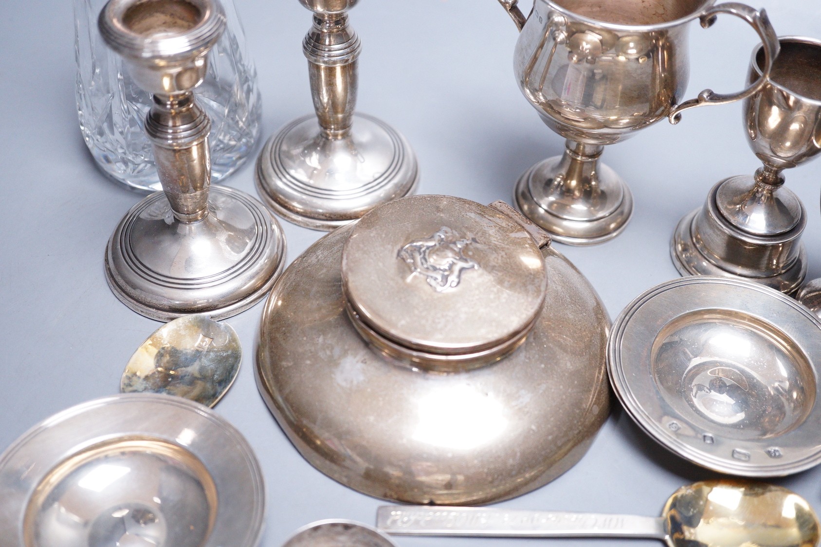 A small collection of assorted small silver, including a capstan inkwell, pair of dwarf candlesticks, two small trophy cups, egg cup, flatware, napkin ring, glass caster, a modern parcel gilt silver stag brooch and three